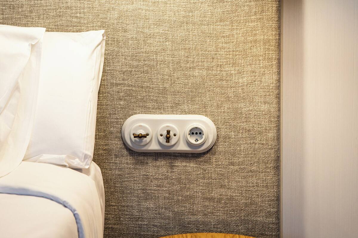 A hotel room with a bed, a round wooden table, and a wall-mounted power outlet.