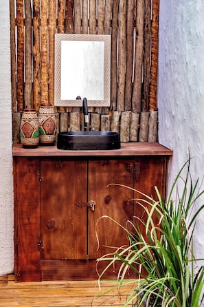 A rustic wooden cabinet with a black sink and a mirror above it. There are two decorative vases and a black basin on the counter.