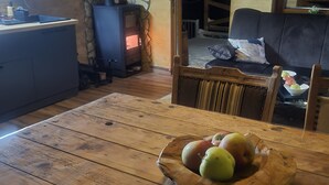 Een houten eettafel met een schaal fruit, een stenen muur, een open haard en een gezellige zithoek.