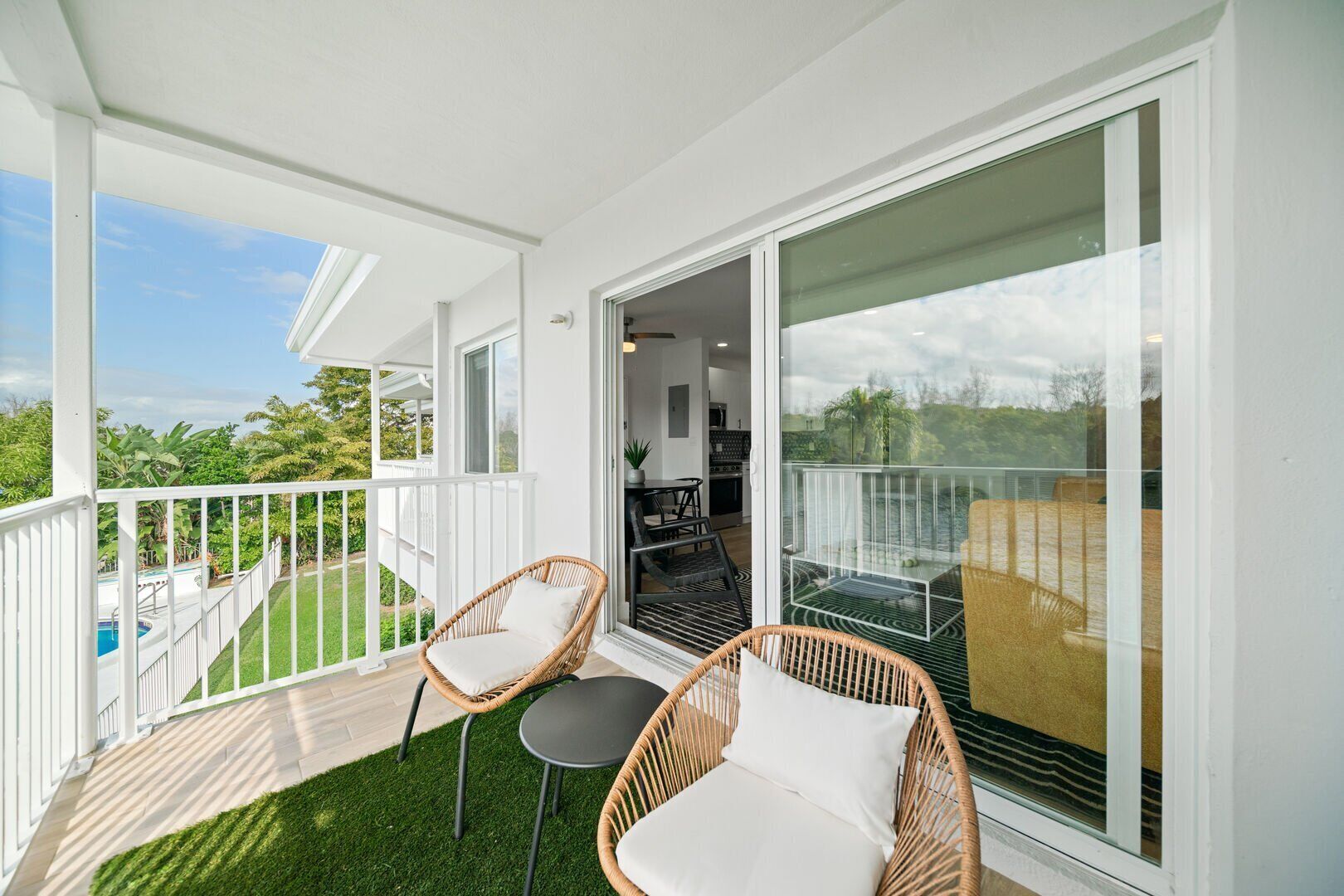 A balcony with wicker chairs, a small table, and a glass door leading to a pool area.