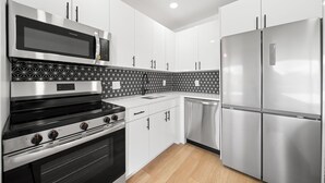 A modern kitchen with stainless steel appliances, white cabinetry, and patterned backsplash. - 261 #13 Managed by Brampton Park (Deerfield Beach)