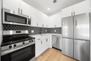 A modern kitchen with stainless steel appliances, white cabinetry, and patterned backsplash. - 261 #13 Managed by Brampton Park (Deerfield Beach)