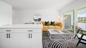 A modern living room with a sofa, a coffee table, and a kitchen area visible through a glass door. - 261 #13 Managed by Brampton Park (Deerfield Beach)