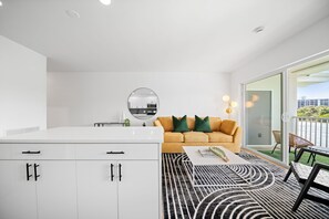 Un salon moderne avec un canapé, une table basse et un coin cuisine visible à travers une porte vitrée.