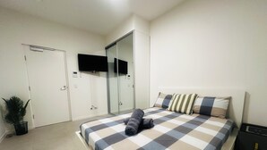 Un dormitorio con una cama, un televisor de pantalla plana montado en la pared, un armario y una mesita de noche.