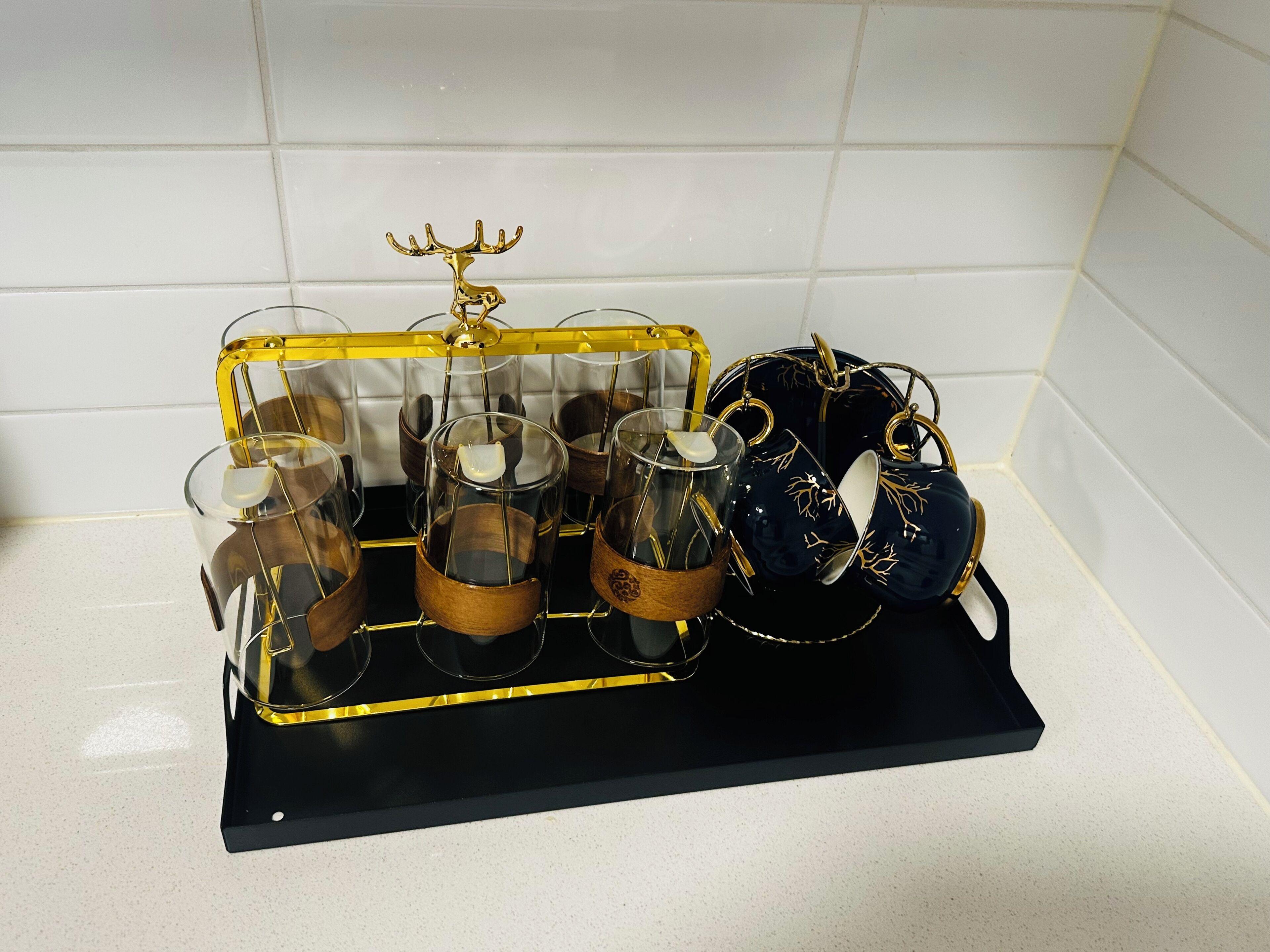 Een zwarte dienblad met een gouden hertenbeeldje, waarop verschillende glazen bolen en een zwarte mok met gouden decoratie staan.