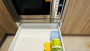 Un cajón de cocina con un microondas encima, que contiene una esponja, un paño y un objeto envuelto.