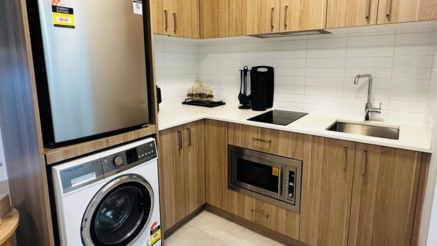 Una cocina compacta con armarios de madera, un refrigerador de acero inoxidable, una lavadora integrada, un microondas y un lavamanos.
