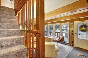 A wooden staircase with carpeted steps leading to a room with large windows, a bench, and a door with a wreath. - Entire cabin duplex one block from ski lifts, bike path, and hiking. (Anchorage)