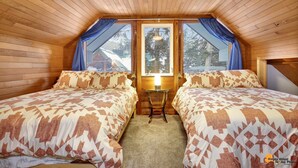 Ein gemütliches Schlafzimmer im Dachgeschoss mit zwei Betten, einem kleinen Tisch und einem Fenster mit Vorhängen.