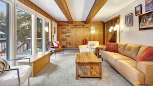 Ein gemütliches Wohnzimmer mit Holzboden, einem beigefarbenen Sofa, einem weißen Sessel und einem Couchtisch aus Holz.