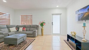 A living room with a grey sofa set, a patterned rug, a decorative vase with flowers, and a flat-screen TV mounted on the wall. - Stylish & Centrally Located Miami Stay / Free Parking & Fast WiFi (Miami)