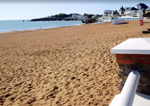 A sandy beach with footprints, a brick wall, and houses in the background. - ECUME  Saint Gilles Croix de Vie (SAINT GILLES CROIX DE VIE)
