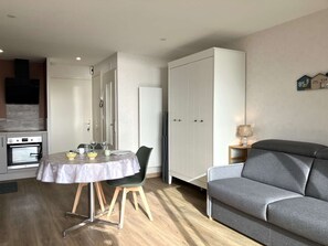 A compact living space with a dining area, kitchenette, and a grey sofa. - ECUME  Saint Gilles Croix de Vie (SAINT GILLES CROIX DE VIE)