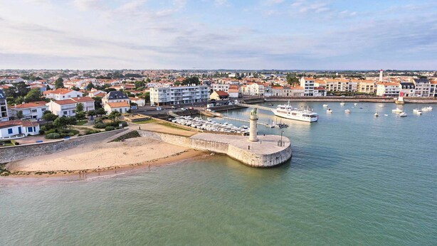 Eine Küstenstadt mit einem markanten Leuchtturm, einer Marina mit Booten und Wohngebäuden.