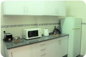 Eine kleine Küche mit weißen Schränken, einer Mikrowelle, einem Toaster, einem Wasserkocher und einem Kühlschrank.