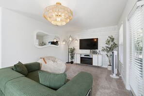 Ein Wohnzimmer mit einem grünen Sofa, einem weißen Schrank, einem Flachbildfernseher und einem Standventilator.