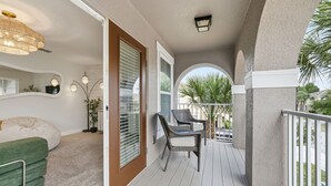 A balcony with a view of palm trees, a wicker chair, and a green couch. - Family-Friendly Villa near Disney! Private Pool & Spa • Gated Resort Community (Davenport)