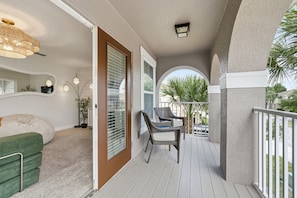 A balcony with a view of palm trees, a wicker chair, and a green couch.