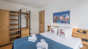 A hotel room with a bed, a wardrobe with multiple shelves, a cityscape painting, and a wooden door. - Rochebrune Ski Terrace - Welkeys (Megève)