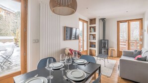 A dining area with a table set for four, a bookshelf, a sofa, and a fireplace. - Rochebrune Ski Terrace - Welkeys (Megève)