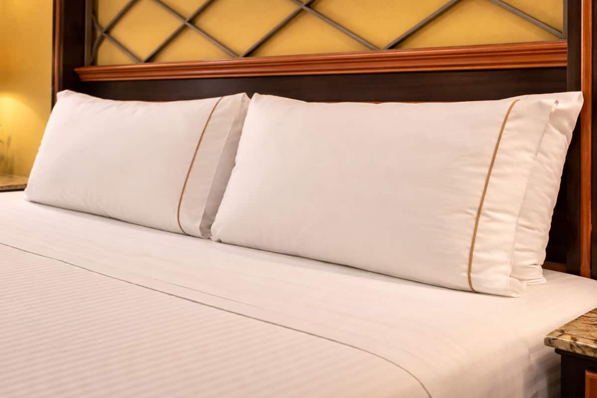 A neatly made bed with white linens and two pillows, a wooden headboard, and a marble side table.