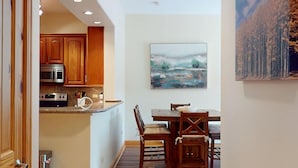 Cocina compacta con armarios de madera, microondas y comedor con mesa y sillas.