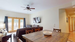Un coin repas avec une table en bois, des chaises, un téléviseur fixé au mur et un ventilateur de plafond.