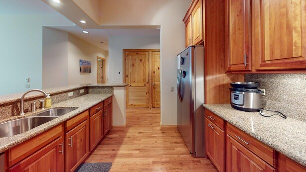 Una cocina con encimeras de granito, armarios de madera, electrodomésticos de acero inoxidable y una puerta de madera al fondo.