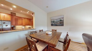 A dining area with a wooden table and chairs, a kitchen with wooden cabinets and a refrigerator, and a painting on the wall. - Ground Floor | Fireplace | Master en-suite | Grande 116 (Angel Fire)