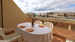 Ein Balkon mit Tisch für zwei Personen, mit Blick auf ein Wohngebiet mit Gebäuden und Palmen.
