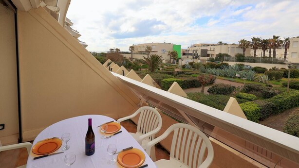 Ein Balkon mit Tisch für zwei Personen, Blick auf einen angelegten Garten und Gebäude im Hintergrund.