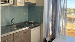 Uma cozinha compacta com micro-ondas, pia e lava-louças, uma mesa de jantar com cadeiras e vista pela janela com cortinas leves.