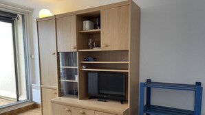 Um quarto com um armário de madeira com vários compartimentos, uma televisão e uma estante azul.