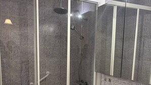 Un bagno con doccia vetrata, lavandino bianco e parete rivestita in piastrelle.
