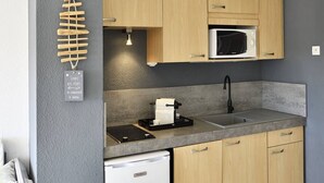 A compact kitchen with wooden cabinets, a built-in microwave, a dishwasher, and a small countertop. - GLOSSY - Studio Héliopolis AB325 - Luxury -2 people (AGDE)