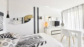 A modern bedroom with a bed, bedside table, and a desk with a chair. - GLOSSY - Studio Héliopolis AB325 - Luxury -2 people (AGDE)