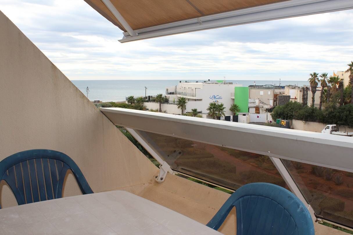 A balcony with a view of the sea, a table, and two chairs.