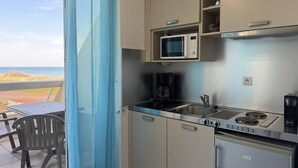 Una kitchenette con microondas, cafetera y estufa, una silla y vista a la playa.