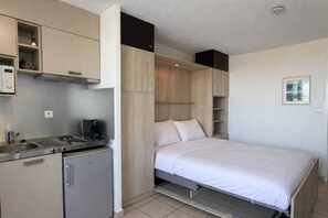 A compact room with a kitchenette, a bed, and built-in storage. - MAKENA - Studio Héliopolis AB330 - Luxury -2 people (AGDE)