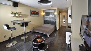 Ein modernes Hotelzimmer mit einem Bett, einem kleinen Esstisch, zwei Barhocker, einem Fernseher und einer Wandklimaanlage.