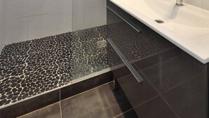 Ein modernes Badezimmer mit einer gläsernen Duschkabine, einem weißen Waschtisch mit schwarzer Arbeitsplatte und einem großen Spiegel.