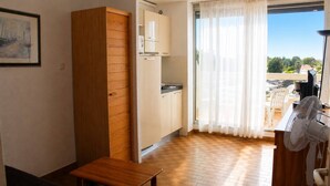 A compact kitchen with a wooden cabinet, a small table, and a sliding glass door leading to an outdoor area with a fan. - Studio Héliopolis AB342 - 2 people (AGDE)