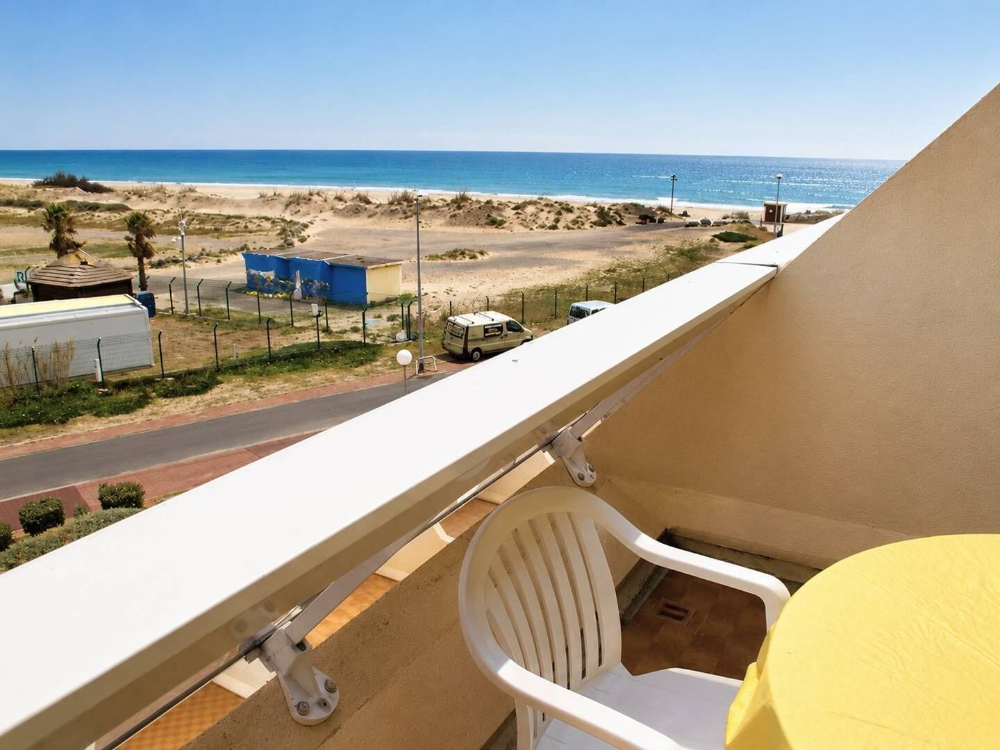 A balcony with a view of the beach, a chair, and a table.