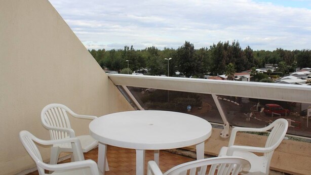 A balcony with a round table and four white plastic chairs, overlooking a residential area with trees and houses. - Studio Héliopolis AB342 - 2 people (AGDE)
