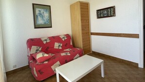 Une pièce avec un canapé rouge, une table blanche et une armoire en bois.
