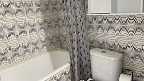 Une salle de bain avec un papier peint à motifs, une baignoire, des toilettes et un meuble de rangement.