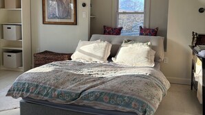 Een slaapkamer met een schuine kap, een bed met bloemenbedrijf, een lijstwerk schilderij, en een raam met uitzicht.