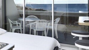 Una habitación moderna con un ventanal grande con vista al mar, una cama y una pequeña mesa con sillas.