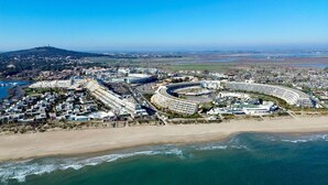 Un resort costero con un hotel en forma de media luna, frente a la playa y vistas del paisaje circundante.